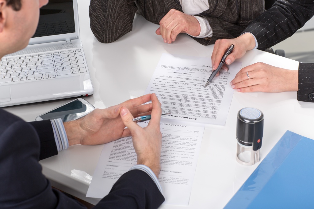 Three people sitting at a table signing documents, hands close-up